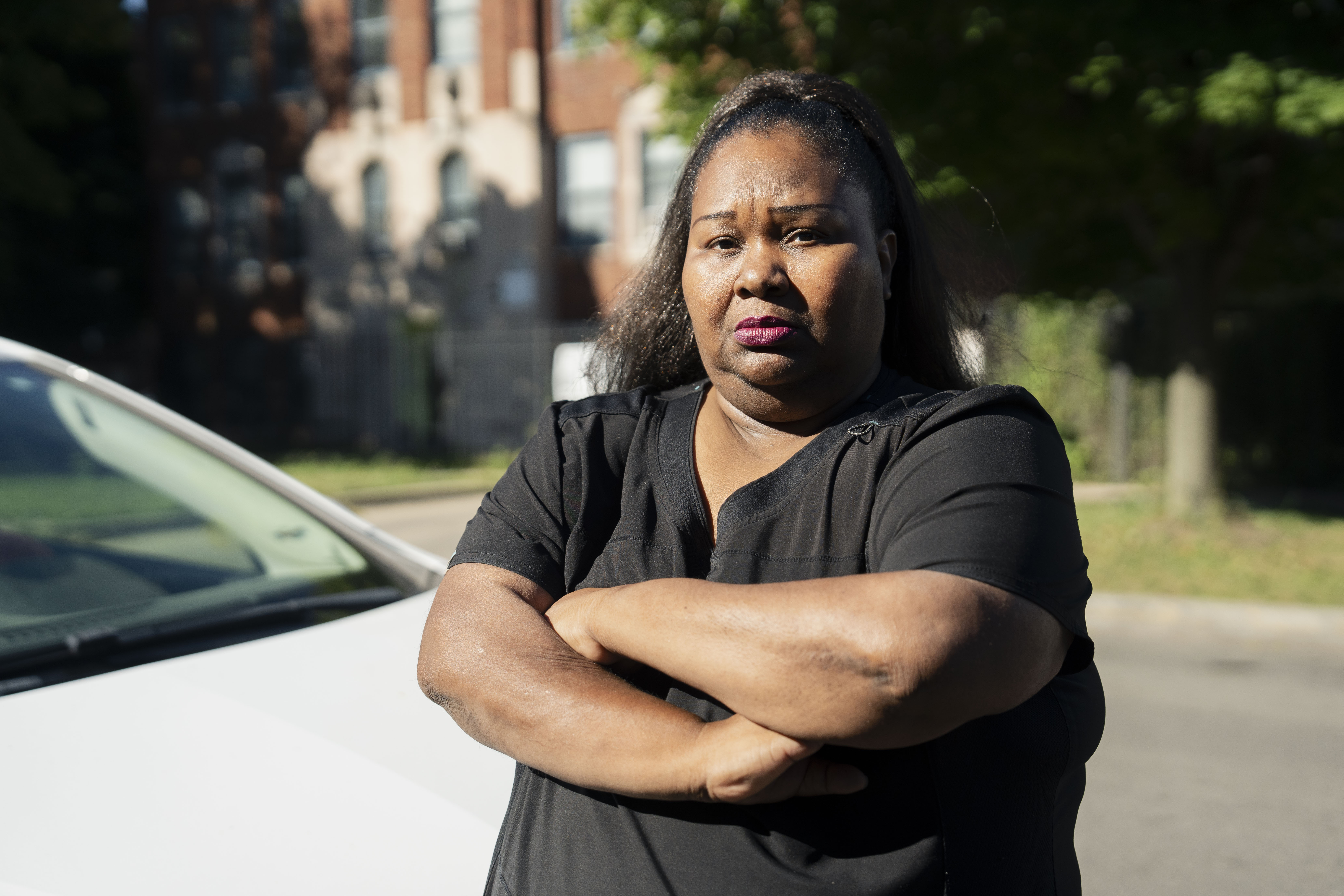 Austin resident Angela Crosby, a home health aide, stands beside her car, which was damaged in a wreck in 2021. Crosby hasn