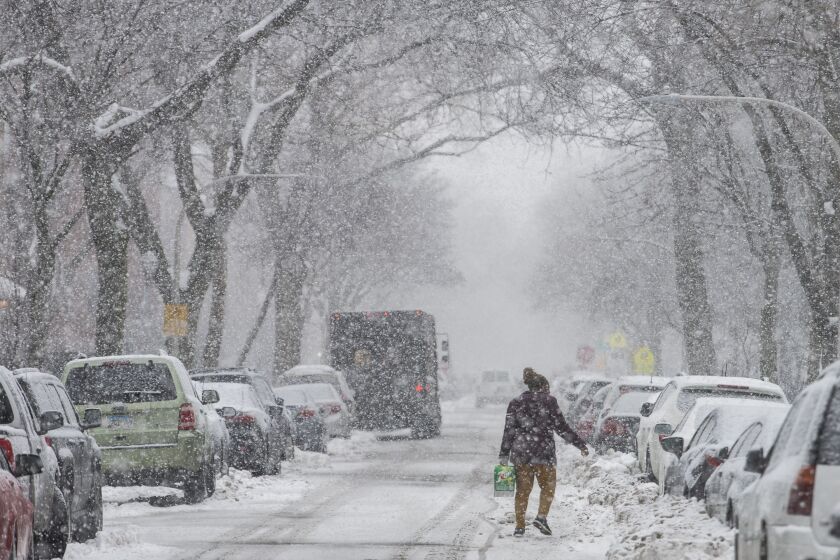 A woman walks in the middle of the street carrying a case of soda to her apartment on N. Winthrop Ave., as heavy snowfall blankets Chicago’s Edgewater neighborhood, Thursday, Feb. 4, 2021.