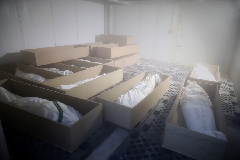 Several rectangular cardboard boxes are on the floor. Inside the boxes are bodies of young children wrapped in white cloth.