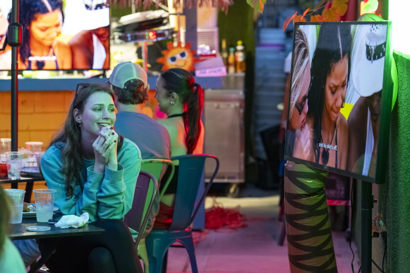 A woman watches a TV screen showing an episode of "Love Island USA," at the back patio of restaurant Tacotlan.
