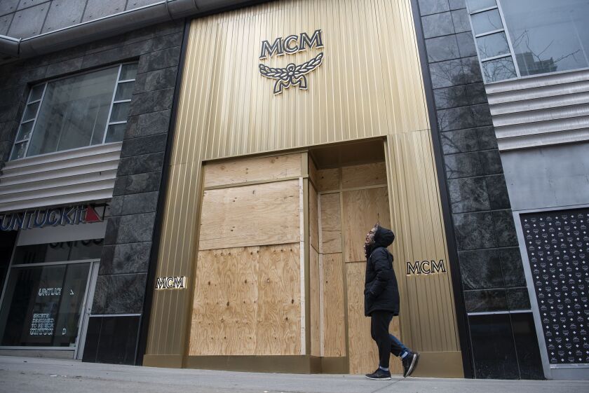 A person walks on Saturday in front of the boarded up windows of MCM, a luxury travel goods store at 540 N. Michigan Ave.