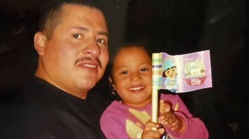 A man to the right is holding a little girl in pink holding a colorful flag.