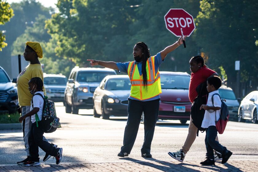 A crossing guard helps students and parents cross the street Monday as they arrive at Willa Cather Elementary School for the first day of school.