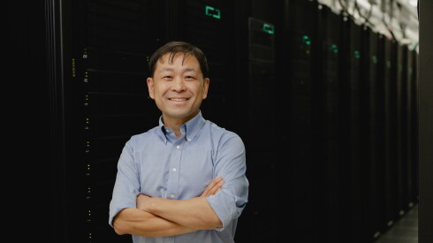 A smiling Kaiyu Guan in front of a bay of servers.
