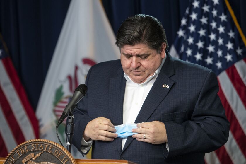 Gov. J.B. Pritzker puts away his face mask before delivering his daily Illinois coronavirus update in April of 2020.