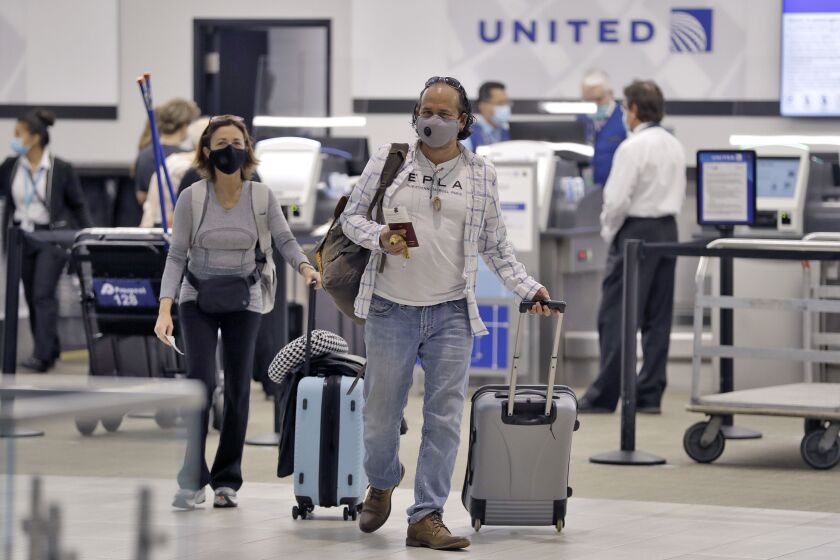 Two passengers wearing face masks and pulling their suitcases walk away from a United Airlines ticket counter on June 16 in Tampa, Florida. Airline travel is still down significantly and United is considering furloughing 36,000 employees.