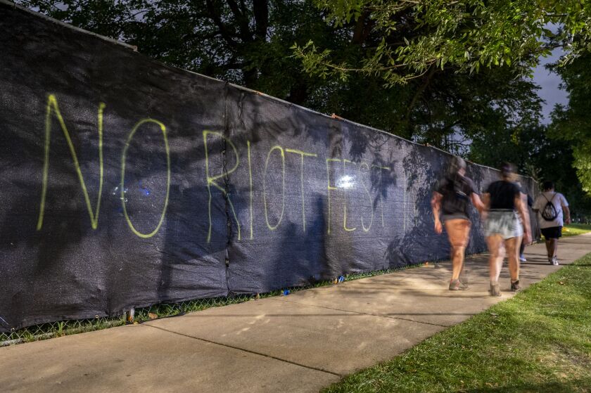 Festivalgoers walk by graffiti that reads “NO RIOT FEST IN OUR PARK” along the Riot Park fence in Douglass Park, Sunday, Sept. 18.