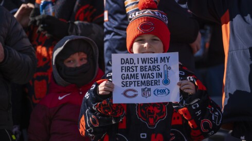 A young Chicago Bears fan holds a sign that reads, "Dad, I wish my first Bears game was in September!"