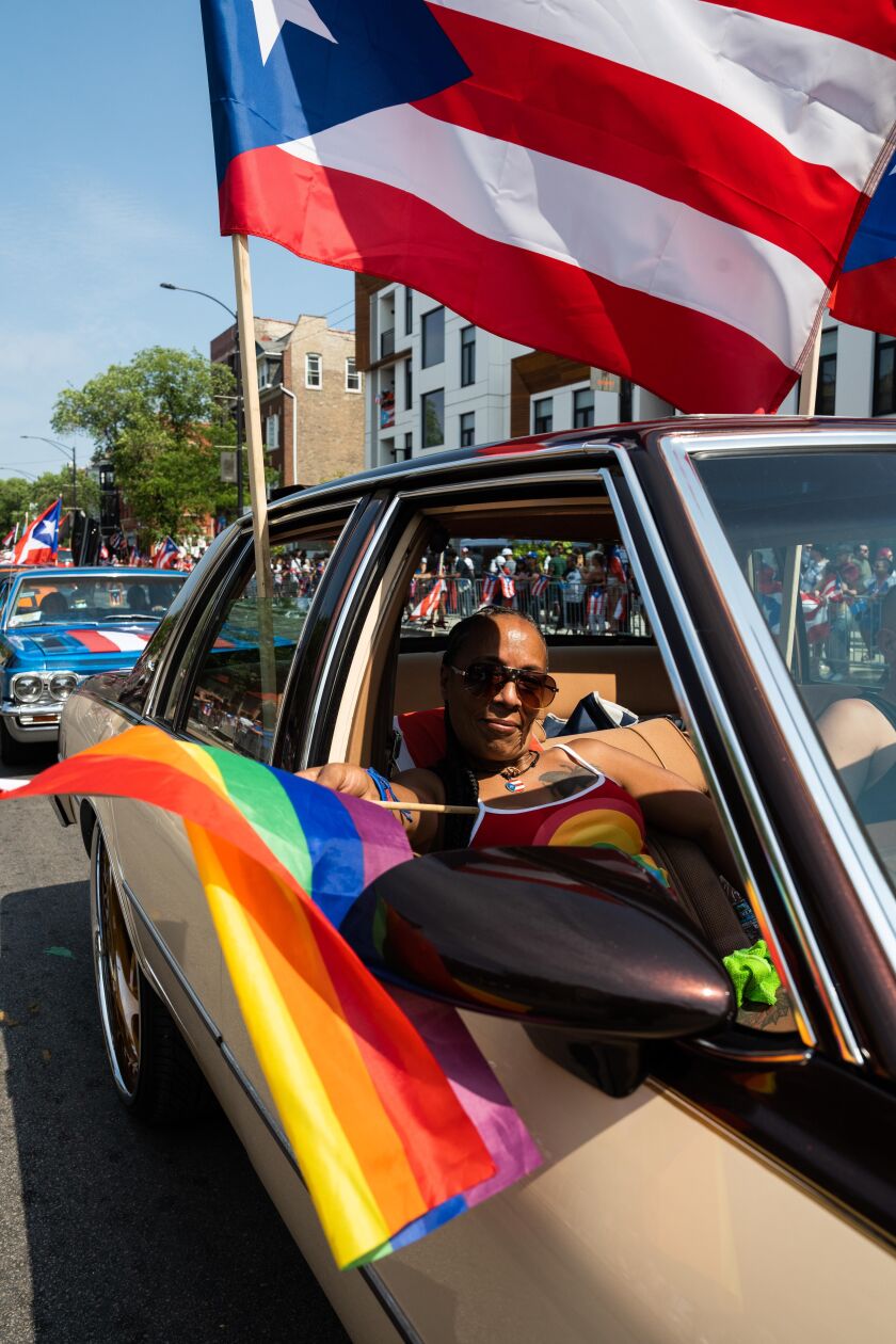 A parade goer in a lowrider car waves a rainbow flag during the Puerto Rican People’s Day Parade Saturday.