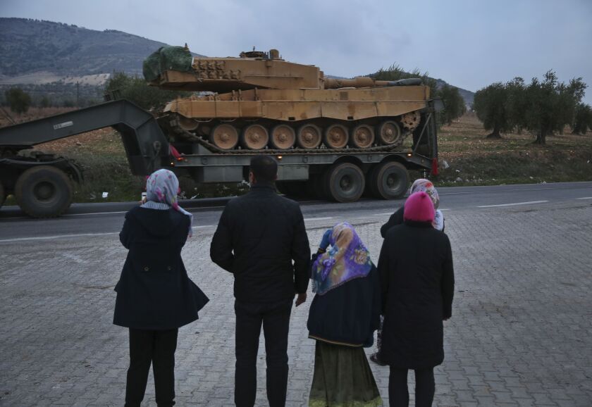 Residents watch as a truck, part of a convoy, transporting a Turkish Army tank is driven in the outskirts of the town of Kilis, Turkey, near the border with Syria, on Sunday. | AP Photo