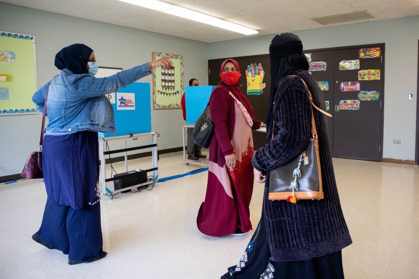 Rehana Ahmed, left, shows Bibi Sabura, center, who is voting for the first time, where to go to cast her ballot at the Warren Park Field House on Tuesday.