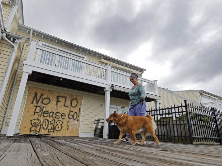 Barbara Timberlake walks with her dog, Danny, past a boarded up store on the river front in downtown Wilmington, N.C., as Hurricane Florence threatens the coast Thursday, Sept. 13, 2018. | AP Photo