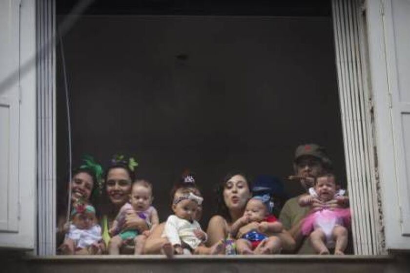 People and babies wearing carnival costumes watch the ‘Ceu na Terra’, or Heaven on earth, carnival parade from the window of a house in Rio de Janeiro, Brazil, Saturday, Feb. 7, 2015. (AP Photo/Felipe Dana)