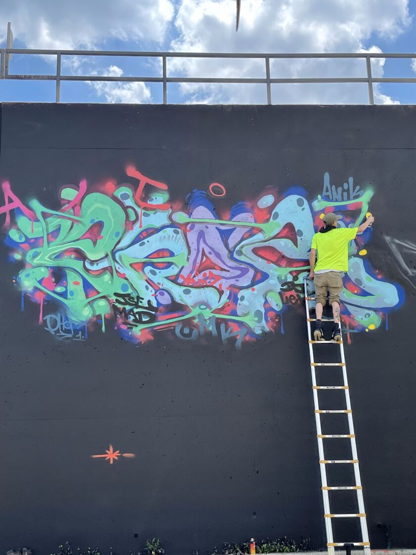 An artist works on the 49th Street retaining wall in August during a three-day
