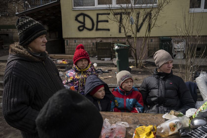 People wait for a free food delivery in Bucha, on the outskirts of Kyiv, Ukraine. The graffiti written by the neighbors on the wall in the background indicates