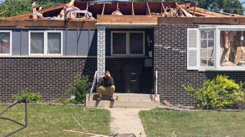 A man holds his head while sitting outside a storm-damaged home near 192nd Place and Oakwood Avenue in Lansing on July 29.