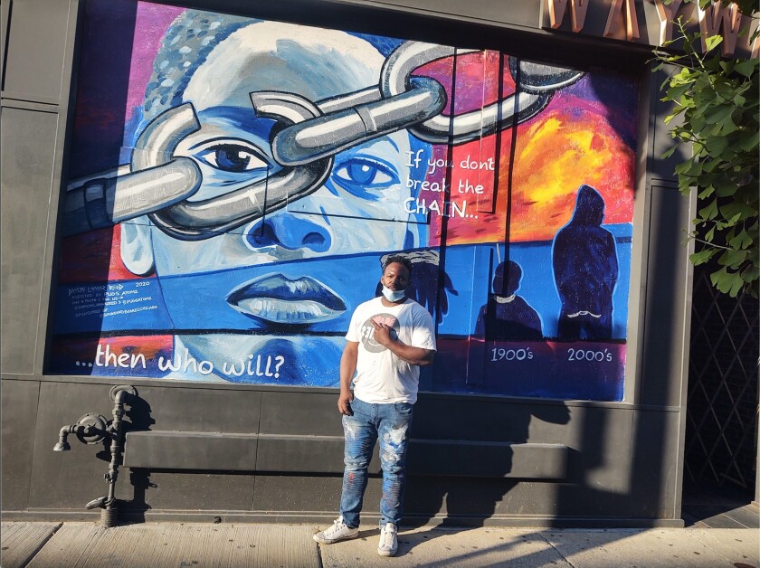 Street artist Damon Lamar Reed, 42, of Woodlawn, in front of his mural “If you don’t break the chain, then who will?” outside Wayward in Wicker Park. In it, Reed portrays systemic racism as a chain on Black people.