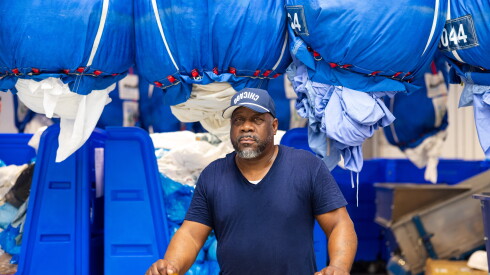 Ronald "Ron" Vann at Fillmore Linen Service in North Lawndale stands in front of bins of commercial laundry.