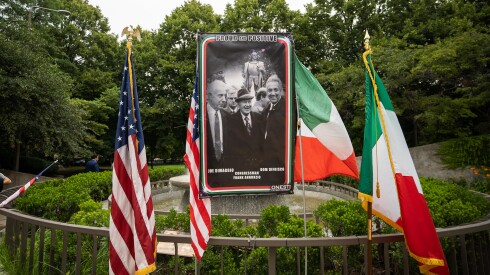 A poster of Italian Americans stands, surrounded by Italian and American flags, in the spot where a statue of Christopher Columbus once stood in Arrigo Park in Little Italy.