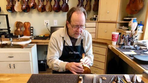 A man applies a woodworking tool to a disassembled violin.