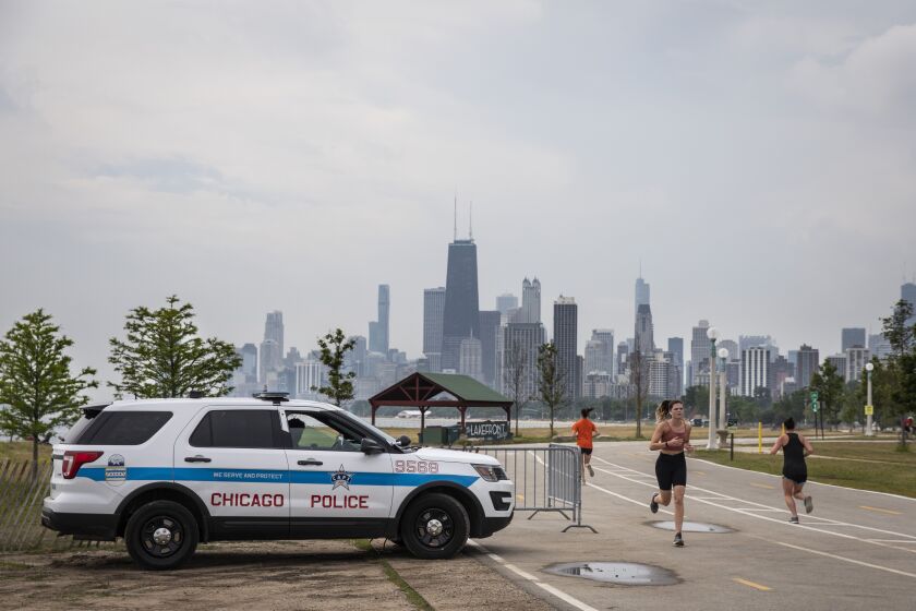 A Chicago Police officer keeps watch as people exercise on the Lakefront Trail near Fullerton Avenue on the North Side on Monday, the first day the park reopened to the public after being closed amid the coronavirus pandemic,