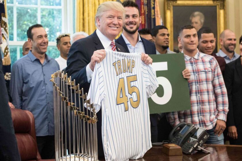 US President Donald Trump poses with a jersey given to him by members of the Chicago Cubs baseball team in the Oval Office at the White House in Washington, DC, on June 28, 2017. / AFP PHOTO