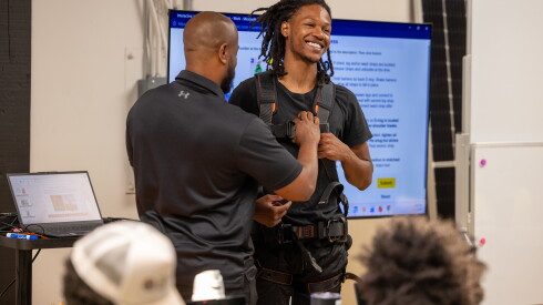 JIREH instructor Kevin Perry and student Javon Burns demonstrate how to wear a safety harness, during class.