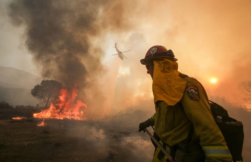 A firefighter watches as a helicopter makes a drop on a wildfire near Placenta Caynon Road in Santa Clarita, California on Sunday. | Ringo H.W. Chiu/AP
