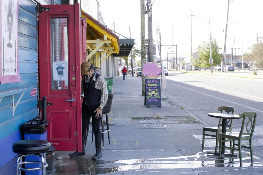 A man stands by a door on St. Claude Avenue in New Orleans, where the toll of the coronavirus pandemic on this year’s toned-down Mardi Gras is evident.