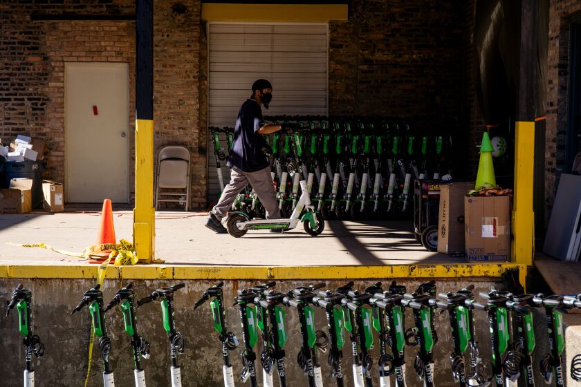 A worker wheels a Lime scooter into a warehouse in West Town Wednesday morning, Aug. 12, 2020. Lime deployed 1,000 scooters across Chicago Wednesday.