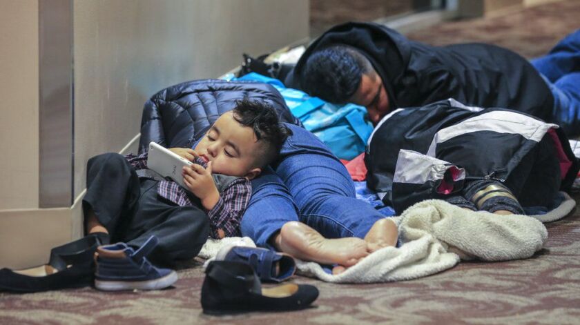 Kenneth Reyes, 2, watches phone cartoons as his parents, Lucas and Areli and sister, Yosselyn, 11, sleep on the second floor of the atrium overnight into Monday morning, Dec. 18, 2017, at the airport. | John Spink/Atlanta Journal-Constitution via AP