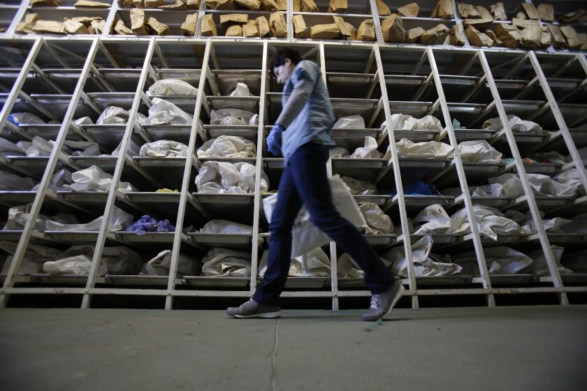 In this photo taken Sunday, senior forensic anthropologist Dragana Vucetic walks inside a facility where are more than 4,500 body-bags containing mortal remains recovered from mass graves from the Bosnian war wait to be identified, in Tuzla, Bosnia and He