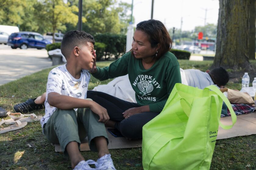 Eliannys Piña, an asylum-seeker from Venezuela, wipes the face of her 9-year-old son, Elias, as the family sits outside the Grand Crossing District police station on the South Side, Monday, Aug. 21. Elias and his 6-year-old sister said they were turned away from a Chicago Public School on the district’s first day.