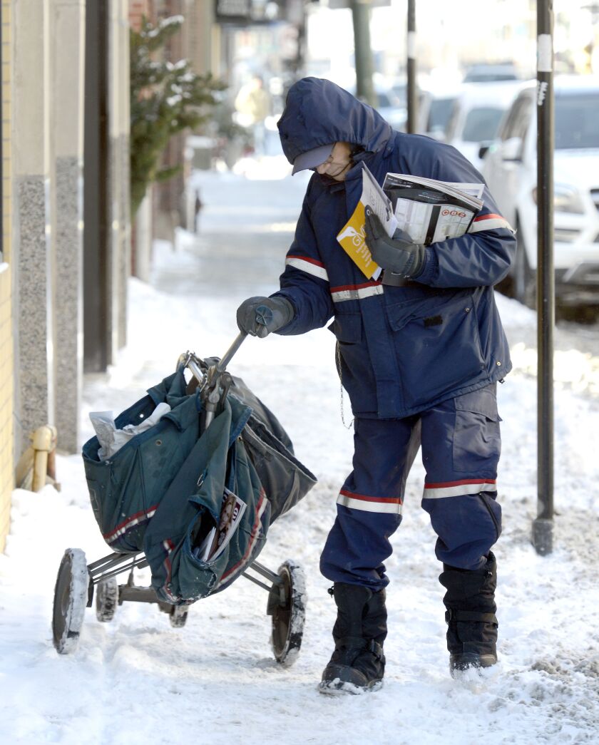 Postal worker Rafael Matos struggles a bit with his cart on the snow-covered sidewalk while delivering the mail Tuesday afternoon on Fullerton Avenue. “This is rough. It makes it a little harder for us to move,” he said. It’s also difficult to sort the ma