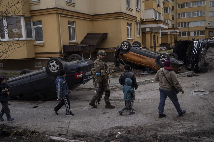 A Ukrainian soldier walks in Bucha with children passing cars destroyed during the war against Russia.