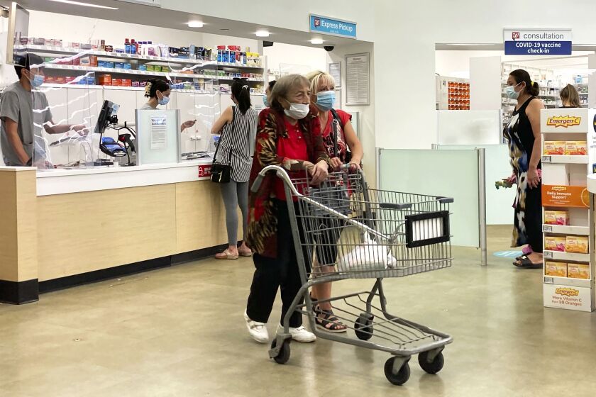 People wearing masks shop and wait in line at a Walgreens in Wheeling. A rush of COVID-19 vaccine-seeking customers and staff shortages are squeezing drugstores around the country.