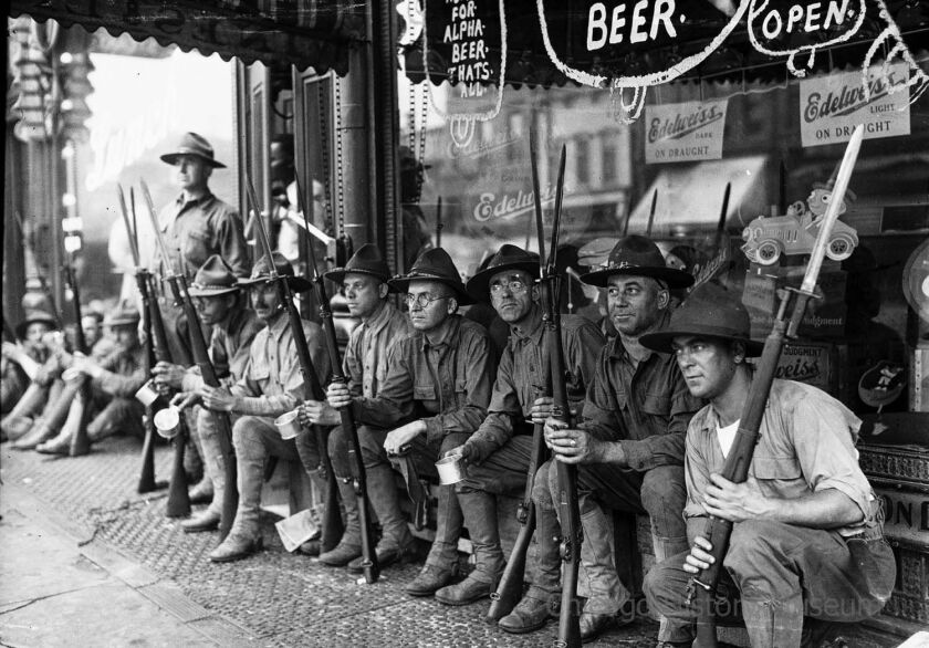 A row of armed National Guard sitting in front of a storefront during the race riots in Chicago, Illinois, 1919. | Jun Fujita/Chicago History Museum