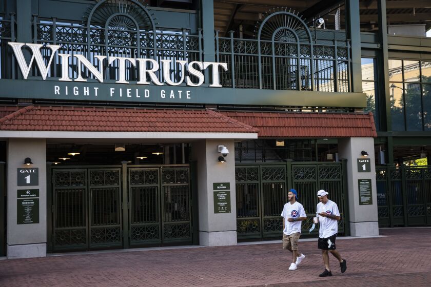 Fans walk by closed gates at Wrigley Field shortly before the start of the opening day game between the Chicago Cubs and the Milwaukee Brewers, Friday evening, July 24, 2020.