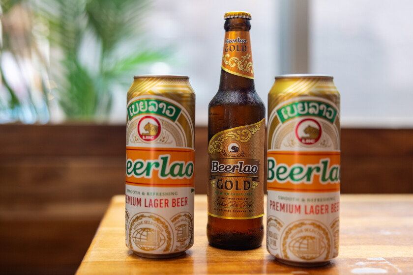 Two tall cans and a bottle of Beerlao on a wooden table.
