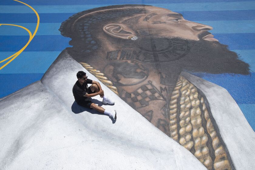 In this April 17, 2019 photo, mural artist Gustavo Zermeno Jr. poses for photos on a basketball court mural he dedicated to slain rapper Nipsey Hussle in Los Angeles. | AP Photo/Jae C. Hong