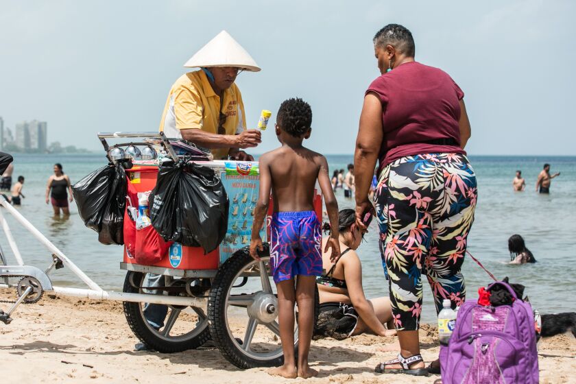 A “paletero” or ice cream vendor hands a popsicle to a child at Montrose Beach as temperatures rise to 95 degrees.