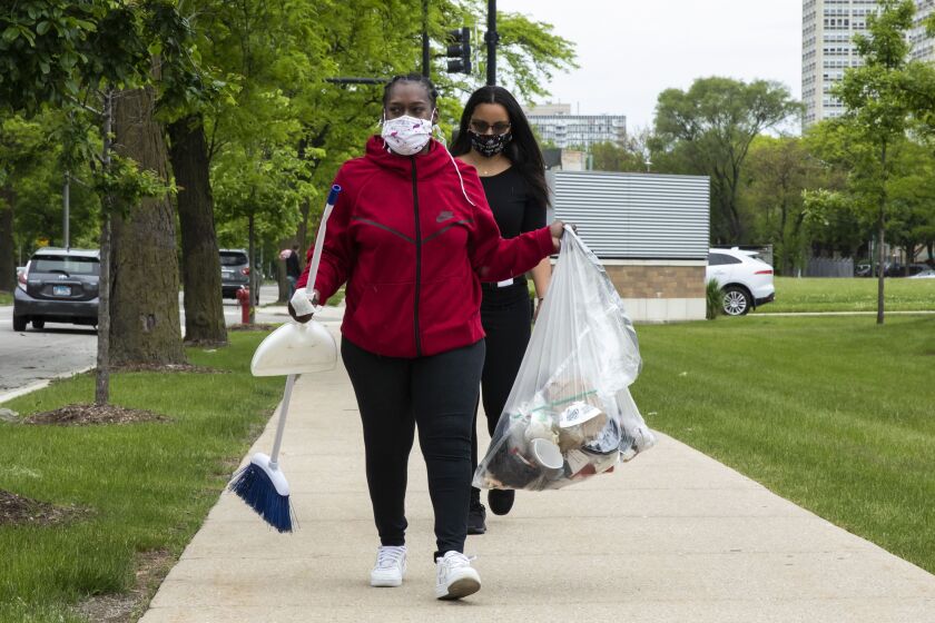Marquita Williams, center, 26, of Bronzeville, cleans litter outside a Mariano’s at 3857 S. Martin Luther King Dr. after the grocery store was looted, Monday morning, June 1, 2020.