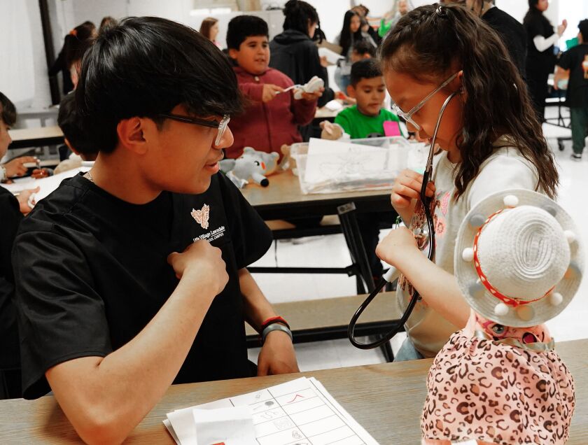 Javier Rodriguez of the Career and Technical Education Health Sciences program at Little Village Lawndale High School, instructs Galilea Saucedo how to use a stethoscope at the teddy bear clinic for students at Eli Whitney Elementary in Chicago Thursday, April 27, 2023.