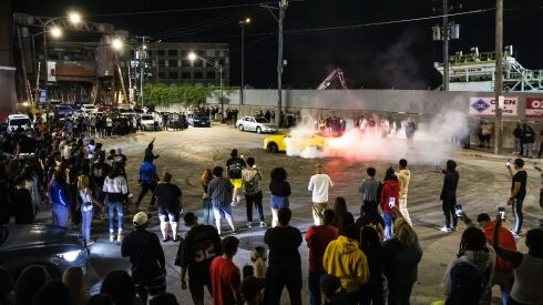 People watch as a car drifts in circles during a takeover in a South Side intersection, Friday night, Aug. 12, 2022.