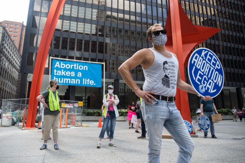 While counter-protesters rally behind him, Jerald Kluting stands with a sign during the “Bans Off My Body” protest Friday afternoon at Federal Plaza in the Loop.