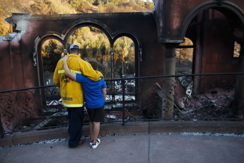 Firefighter Terry Sanders and his son Isaac, 11, who lost their home in a wildfire, comfort each other in front of their neighbor’s home, destroyed by the same wildfire after trying to find sentimental items belonging to the neighbor on Saturday, Oct. 14,