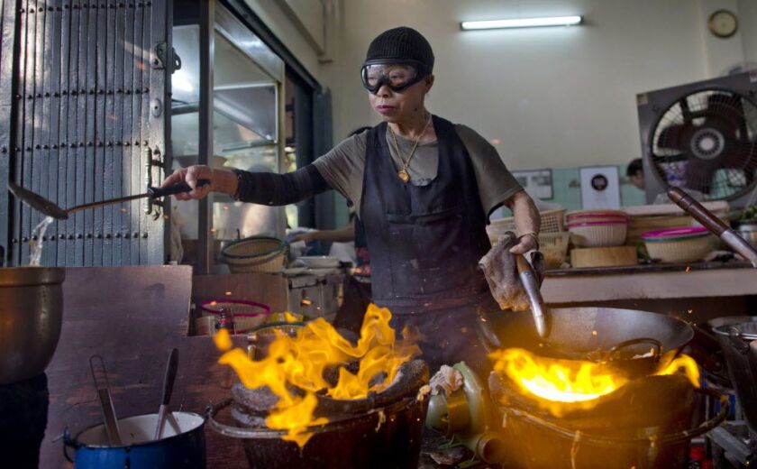 In this Dec. 20, 2017, photo, Thai cook Supinya Jansuta, 72, better known as “Jay Fai,” wearing goggles, cooks with two flaming woks at her eatery in Bangkok, Thailand. | AP Photo/Gemunu Amarasinghe