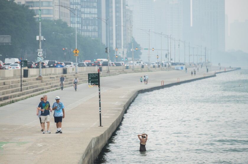Few people walk on the lakefront and swim in Lake Michigan at Ohio Street Beach in Streeterville as the Chicago skyline is obscured by air pollution driven by the wildfires in Canada on Friday.