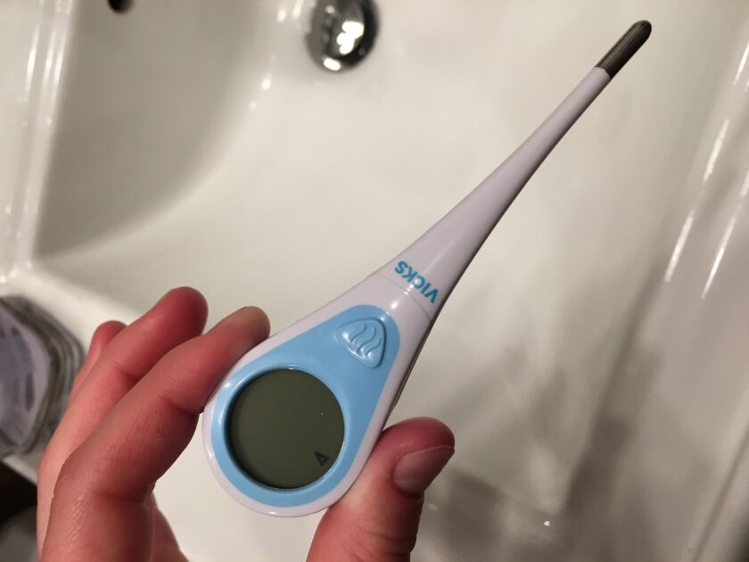A hand is holding a thermometer over a sink in this photo. Personal care thermometers are in high demand as people test themselves for fever during the coronavirus pandemic.