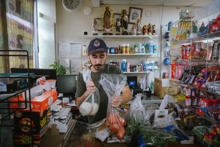 Diego Reynoso weighs vegetables to fulfill a delivery order for a customer at Supermercado Reynoso in Cicero on Sept. 24.